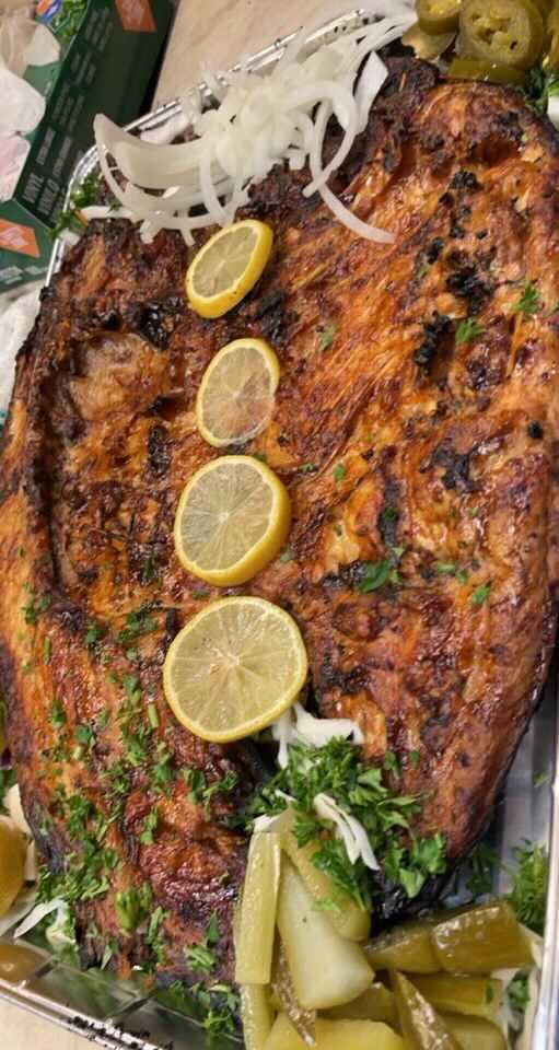 Whole masgoof fish roasting upright beside an open wood fire